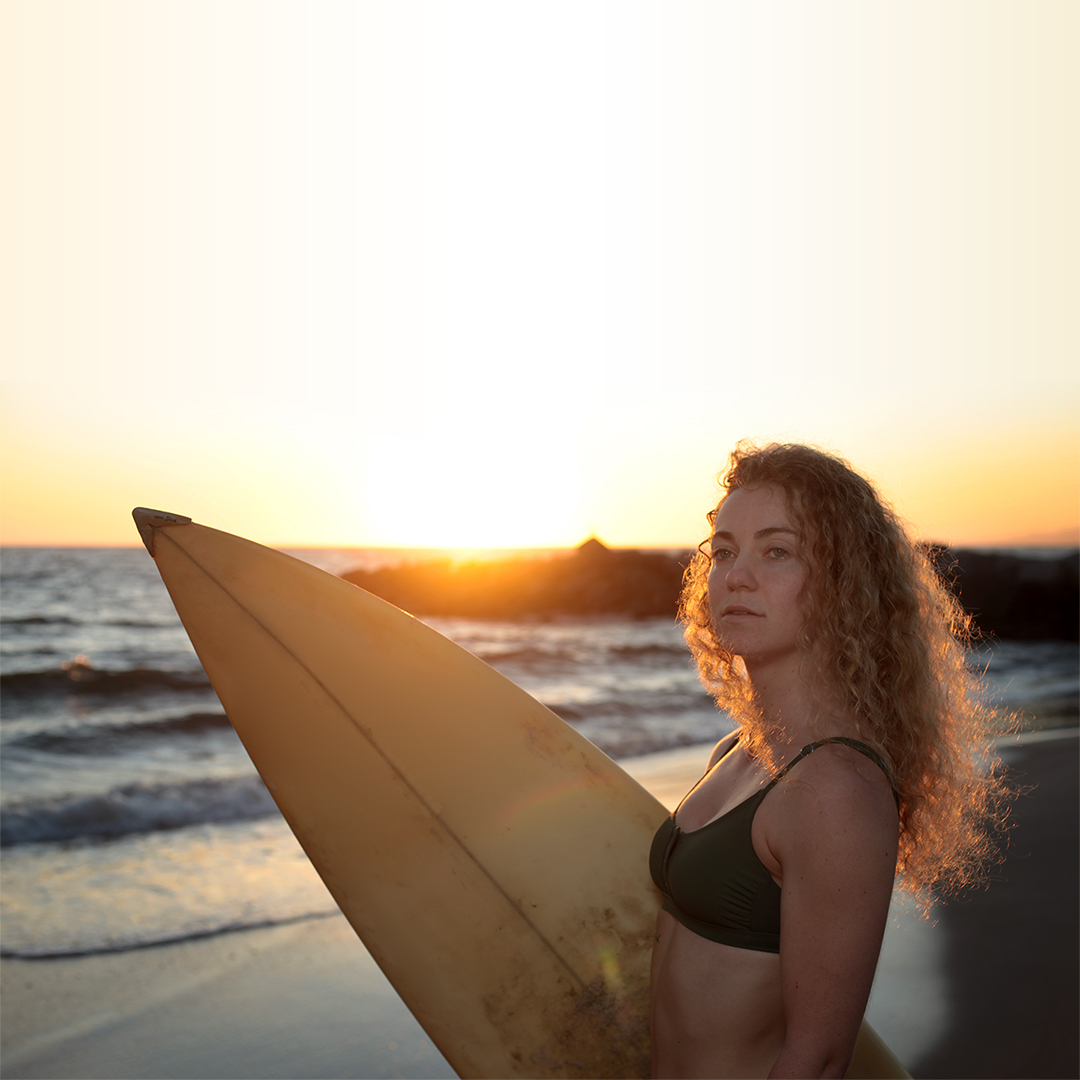 Surfer holding a board at sunset